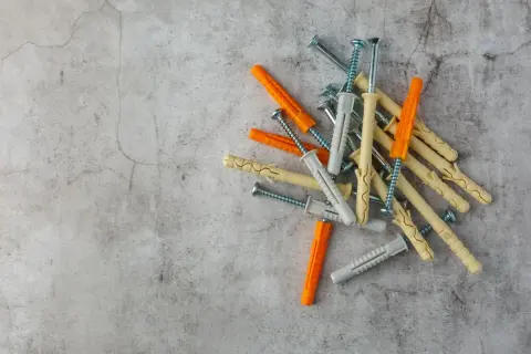Montón de tacos de pared de plástico y tornillos. Hay varios tipos de tacos de pared, de colores naranja, gris y beige, listos para fijar objetos.
