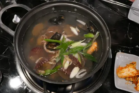 Un plat de cuisson de fruits de mer mijote dans un bouillon, avec des moules, des crevettes, des pétoncles et des poulpes.