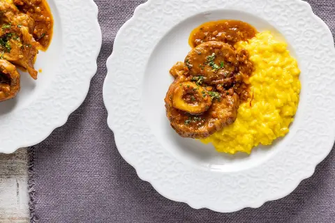 Ossobuco ricetta originale servito su un piatto bianco con risotto giallo allo zafferano.