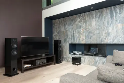 Nowoczesny salon z telewizorem, głośnikami i czarnym subwooferem. To właśnie subwoofer co to, urządzenie wzmacniające niskie tony.