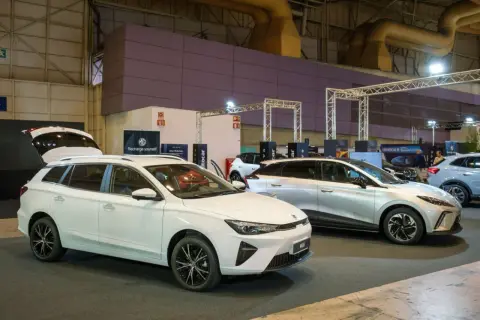 Białe kombi MG5 z otwartą klapą bagażnika i srebrny SUV MG na wystawie samochodowej.