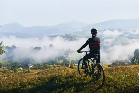 Rowerzysta podziwia mglisty krajobraz dolnośląskiej krainy rowerowej. W oddali góry i malownicze wioski.