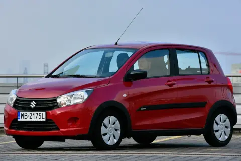 Czerwony Suzuki Celerio z kierowcą za kierownicą, zaparkowany na zewnątrz.