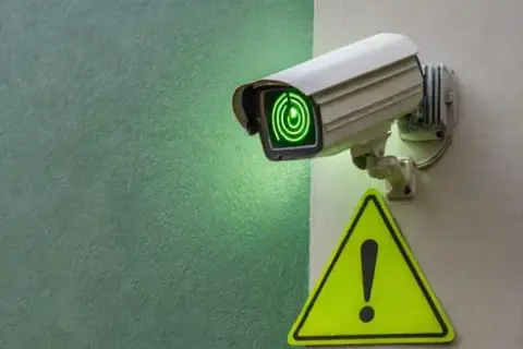 Caméra de vidéosurveillance allumée, prête pour la maintenance. Un panneau de signalisation jaune avec un point d'exclamation est visible à proximité.