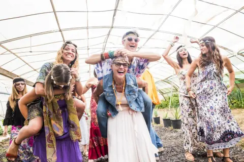 Grupa przyjaciół w stylu hippie świętuje w szklarni, śmiejąc się i bawiąc.