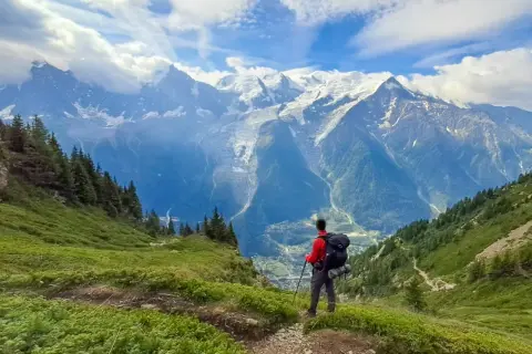Randonneur contemplant les majestueuses montagnes enneigées, un paysage digne des **Vosges** en été.