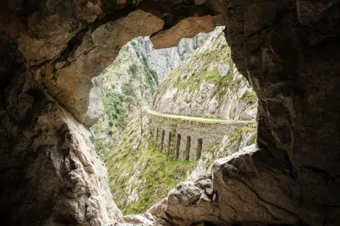 Vista desde una cueva de la ruta del Cares, con un camino tallado en la roca y arcos de piedra.