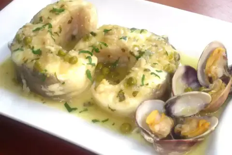 Congrio en salsa verde con guisantes y almejas, un plato delicioso y lleno de sabor.