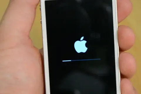 Dłoń trzyma iPhone'a z logo Apple i paskiem postępu, wskazującym na proces hard reset iPhone.