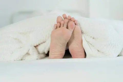 Pieds sous une couverture douillette, prêts pour un point massage pied pour dormir paisiblement.