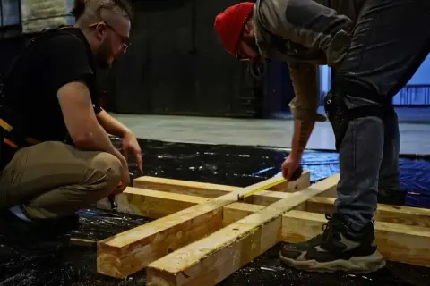 Dwóch mężczyzn planuje, jak połączyć belki drewniane, mierząc je taśmą.