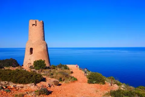 Torre defensiva en la costa, un lugar ideal que ver en Gata, con el mar azul de fondo y visitantes disfrutando del paisaje.