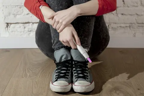 Młoda dziewczyna w dżinsach i trampkach trzyma test ciążowy. To trudny moment, kiedy dzieci mają dzieci.