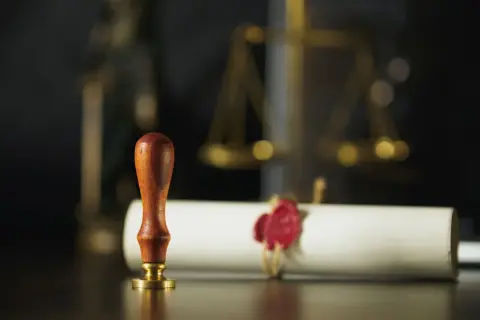 Pieczęć i zwój z czerwonym woskiem, symbolizujące formalności prawne, takie jak wniosek o stwierdzenie nabycia spadku. W tle waga sprawiedliwości.