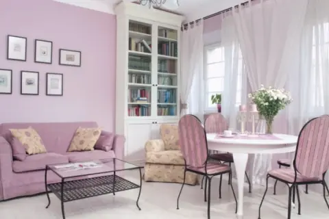 Jasny salon z fioletową kanapą i krzesłami w różowe pasy. Kolor lawendowy ścian świetnie komponuje się z bielą mebli i zasłon, tworząc przytulną atmosferę.