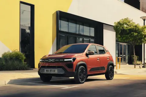 Pomarańczowa Dacia Spring na tle nowoczesnego budynku. Sprawdź atrakcyjną dacia spring cena i wybierz swój wymarzony samochód elektryczny.