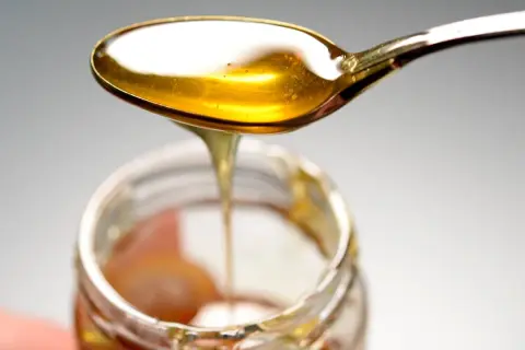 Ein Löffel mit goldenem Honig tropft in ein Glas. Hoffentlich kein schlechter Honig gegessen!
