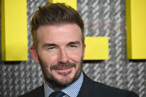 David Beckham sfoggia un taglio corto elegante uomo, con barba curata e un sorriso accattivante.