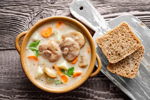 Aksamitna zupa z maślaków z kawałkami ziemniaków i marchewki, podana z chlebem na drewnianym stole.