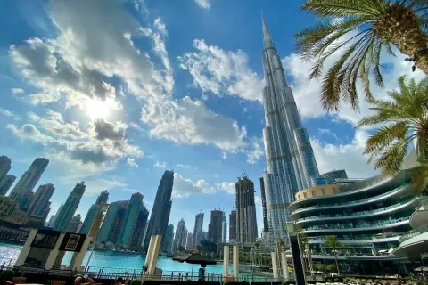 Burdż Chalifa góruje nad Dubajem. Zdjęcia ukazują drapacze chmur, błękitne niebo z chmurami i palmy.