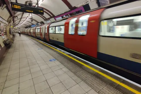 Metro londyn bilet 3 dniowy. Pociąg z czerwonymi i beżowymi elementami mija peron. Na tablicy informacja o odjeździe do Edgware.