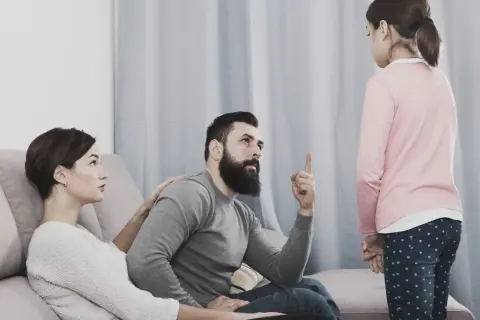 Una bambina ascolta il padre che la ammonisce, mentre la madre, con un'espressione preoccupata, le appoggia una mano sulla spalla, forse per alleviare la sua paura di perdere i genitori.