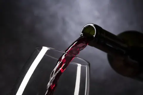 Ciemnoczerwone wino, być może najdroższe wino, leje się z butelki do kieliszka.