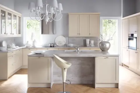 Jasna kuchnia shabby chic z kremowymi meblami, kamiennym blatem i eleganckim żyrandolem.