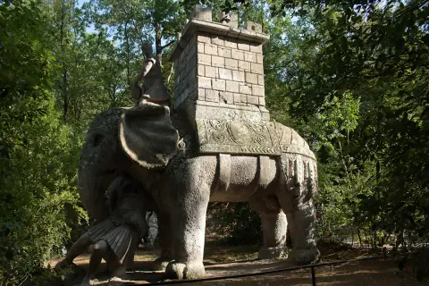 Elefante di pietra con guerriero e torre nel viterbo giardino dei mostri. Un'antica creatura che emerge dal verde.