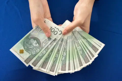 Ręce trzymają stos banknotów 100 zł. Zastanawiasz się, ile dać na 50 urodziny? Taka kwota to dobry początek!