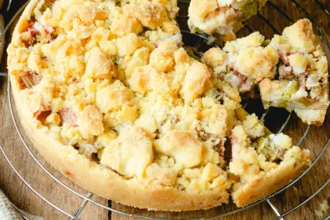 Ein köstlicher Rhabarberkuchen mit Streuseln, der auf einem Gitter abkühlt. Die süßen Streusel bedecken die saftige Rhabarberfüllung.