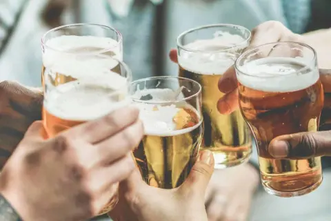 Brindisi con birra, un piacere che, si dice, la birra fa ingrassare. Mani che sollevano bicchieri dorati con schiuma bianca.