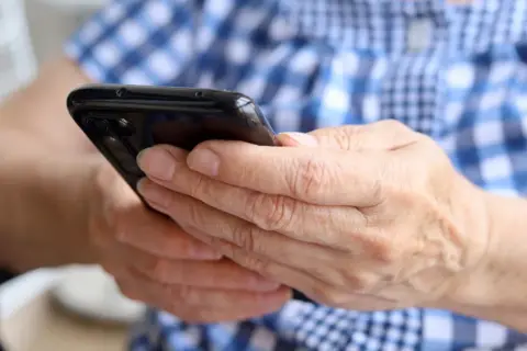Dłonie trzymają czarny smartfon. Zastanawiasz się, jak namierzyć wyłączony telefon?