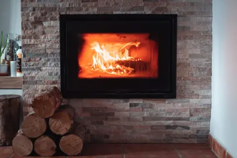 Płonące polana w nowoczesnym kominku, obłożonym kamieniem. Idealne miejsce, by zastanowić się, czy można palić w kominku.