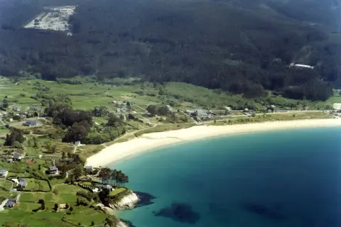 Vista aérea de la playa de Area, Viveiro, con casas dispersas entre verdes colinas y el mar turquesa.