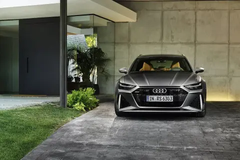 Szary Audi RS6 Avant z beżowym wnętrzem zaparkowany przed nowoczesnym domem. Sprawdź audi rs6 cena.