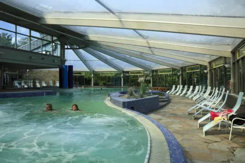 Entspannen in der Therme NRW: Zwei Frauen schwimmen im warmen Wasser unter einem Glasdach, Liegen laden zum Verweilen ein.