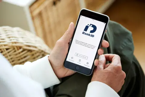 Person håller upp en telefon med BankID-appen öppen, redo för inloggning eller underskrift. Perfekt för din bankID ny telefon.