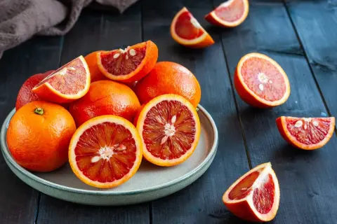 Arancia rossa na talerzu i obok, soczyste, przekrojone na pół, ukazujące intensywny czerwony miąższ.