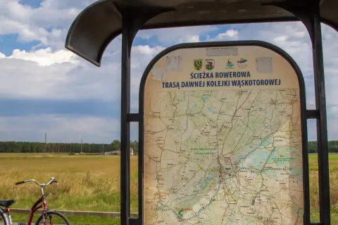 Mapa informuje o ścieżce rowerowej trasą dawnej kolejki wąskotorowej. Obok stoi rower.