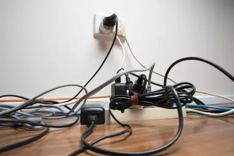 Un enchevêtrement de fils électriques branchés sur une multiprise et une prise murale. Un vrai défi pour faire de l'électricité soi-même sans s'emmêler !