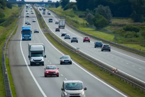 Na autostradzie ruch samochodów. Niebieska ciężarówka wykonuje wyprzedzanie z prawej strony, omijając inne pojazdy.