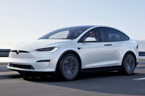 Biały Tesla X w ruchu. Kierowca w okularach przeciwsłonecznych. Sprawdź aktualną tesla x cena i możliwości tego SUV-a.