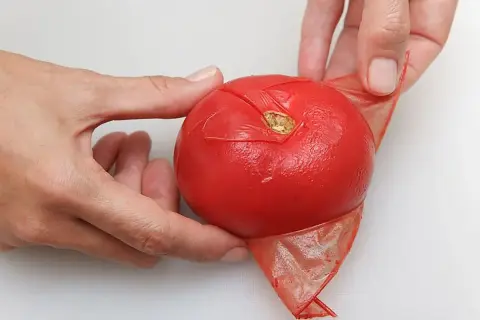 Manos pelando un tomate rojo, mostrando cómo quitar la piel fácilmente.