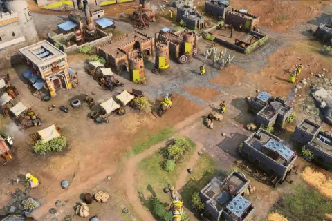 Scena z gry rts: zamek, budynki, rycerze w żółtych strojach, wozy i targowisko.