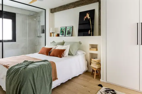 Dormitorio con ducha integrada, cama con mantas cálidas y cuadros. Una reforma sin obras que transforma el espacio con estilo y funcionalidad.