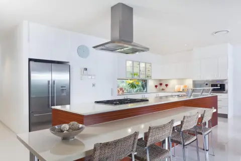 Cocina moderna con isla, nevera de acero inoxidable y campana extractora. Ideal para tu reforma cocina precio.