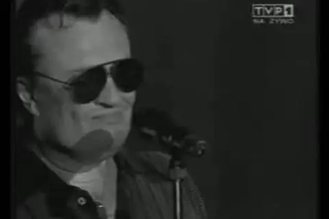 Mężczyzna w okularach przeciwsłonecznych śpiewa do mikrofonu. Widać logo TVP1. A po nocy przychodzi dzień.
