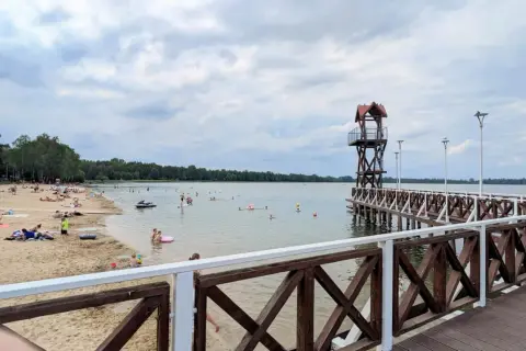Plaża z ludźmi, pomost z wieżą ratowniczą i jezioro w Pogorii.