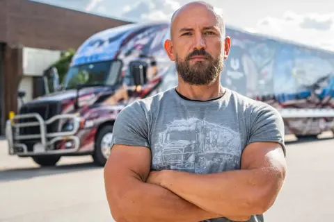 Dawid Andres, w sile wieku, z brodą, stoi przed ozdobioną ciężarówką.